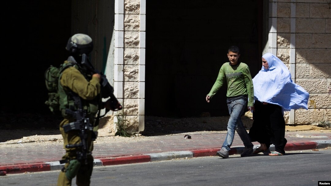 Palestinians walk near an Israeli sold