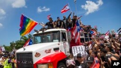 Duduk di atas kap truk, artis penyanyi, Ricky Martin, bergabung dengan selebriti dan demonstran Puerto Rico lainnya dalam protes untuk menuntut pengunduran diri Gubernur Ricardo Rossello, di San Juan, Puerto Rico, 22 Juli 2019. (Foto: dok).