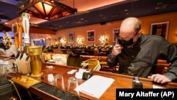 Steve Olsen, the owner of the West Bank Café, reads the specials over the phone to a customer in the empty restaurant. Photo taken on Saturday, Jan. 9, 2021. (AP Photo/Mary Altaffer)