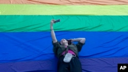 A woman takes a photo of herself while laying on the rainbow flag during a pride march in Belgrade, Serbia, Sept. 7, 2024.