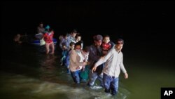 Migrant families, mostly from Central American countries, wade through shallow waters after being delivered by smugglers on small inflatable rafts to U.S. soil in Roma, Texas, March 24, 2021.