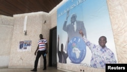 A man walks near a poster showing portraits of former Ivory coast president Laurent Gbagbo (C) and Former Ivory Coast prime minister Pascal Affi N'Guessan (R), leader of Ivorian Popular Front (FPI) at the FPI headquarters in Abidjan, September 2, 2015.