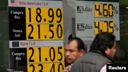 People walk past a board displaying the exchange rate for Mexican peso against the U.S. dollar and the euro in a Bank in Mexico City, Mexico, Nov. 15, 2016. 
