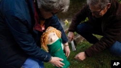 Heather and David Howarth of the 'Hurst Hookers' knitting group adjust a knitted figure of Britain's Camilla, Queen Consort, fitted to a post during a pre-coronation 'yarn bombing' in the village of Hurst, near Reading, England, April 21, 2023.