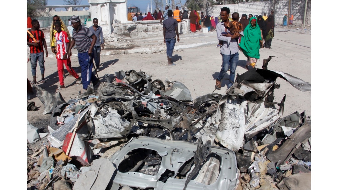 FILE - Somalis walk past debris after a suicide car bomb attack on a government building in the capital Mogadishu, Somalia, Saturday, March 23, 2019. Al-Shabab gunmen stormed the government building after the bomb attack.