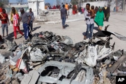 FILE - Somalis walk past debris after a suicide car bomb attack on a government building in the capital Mogadishu, Somalia, Saturday, March 23, 2019. Al-Shabab gunmen stormed the government building after the bomb attack.