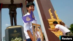 A student holds a portrait of Cambodia's King Norodom Sihamoni (C), after the unveiling ceremony of a statue (back) of the late King Norodom Sihanouk in central Phnom Penh, Oct. 11, 2013. 