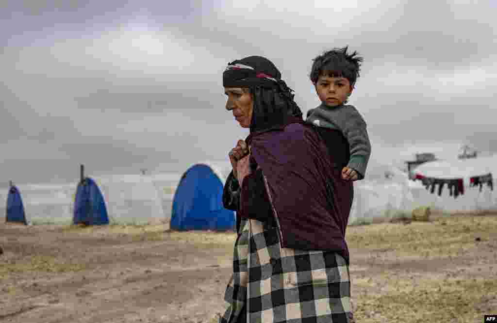 An elderly displaced Syrian woman carries a child in the Washukanni Camp for the internally displaced people near the predominantly Kurdish city of Hasakeh in northeastern Syria.
