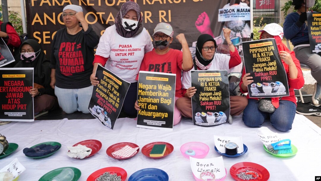 Para aktivis membawa poster-poster dan memamerkan barang-barang rumah tangga dalam demo di depan gedung DPR/MPR untuk menuntut DPR agar mengesahkan RUU Perlindungan Pekerja Rumah Tangga menjadi undang-undang, Jakarta, 14 Agustus 2023. (Foto: Tatan Syuflana/AP Photo)