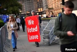 A pro-Brexit protester carries signs outside the Houses of Parliament in London, Sept. 4, 2019.
