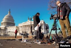 FILE - Members of the news media survey damaged equipment outside the U.S. Capitol a day after supporters of U.S. President Donald Trump stormed and occupied the Capitol in Washington, Jan. 7, 2021.