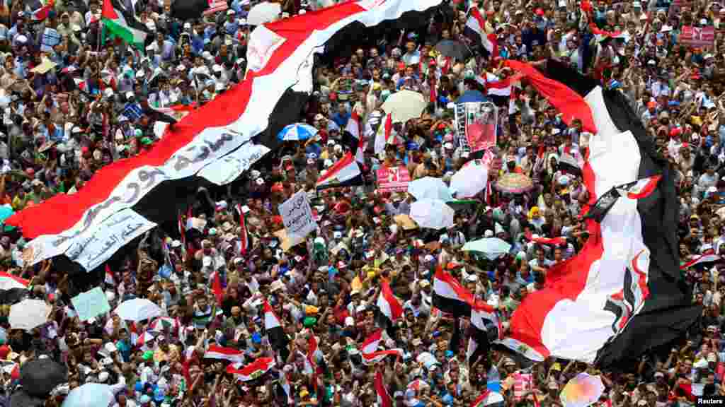  2012年六月二十二号支持穆斯林兄弟会总统候选人穆尔西的民众在开罗解放广场站在巨幅埃及国旗下，抗议延迟宣布埃及总统选举结果。
