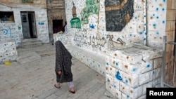 FILE - A Palestinian woman walks outside her home, next to a house (R) purchased by Jewish settlers, in the mostly Arab neighborhood of Silwan in east Jerusalem, October 2014.