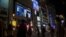 Japanese Prime Minister Yoshihide Suga, on a screen, speaks at a news conference in a live broadcasting shown in a big screen on a building as people walk across an intersection in the Shinjuku district of Tokyo on Thursday, March 18, 2021. Japan…