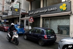 FILE - A man on a scooter passes a branch of the Hezbollah-run Al-Qard al-Hassan banking institution in Beirut, Lebanon, on Jan. 20, 2021.