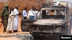 FILE - Security officers and government officials inspect a police car that was burnt during an attack on a convoy escorting the governor of Mandera region Ali Roba outside Mandera town, near Kenya's border with Somalia and Ethiopia, March 13, 2015. 