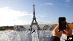 A man jumps on the Trocadero square in front of the Eiffel Tower, where the French artist and photographer known as JR set his artwork, in Paris. 