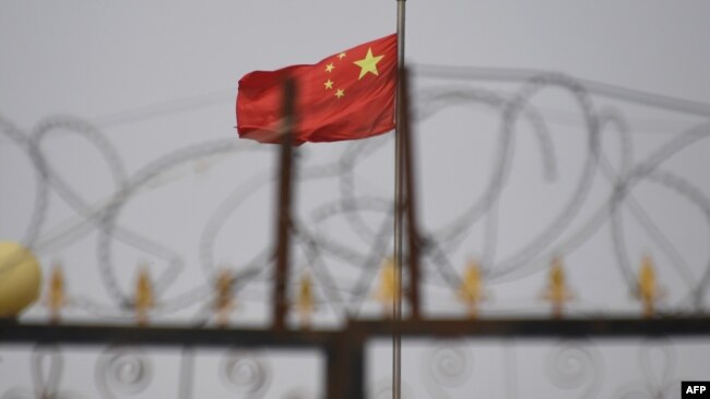 资料照：中国国旗在新疆喀什南部地区一处建筑物的围栏铁丝网后飘扬。（2019年6月4日）