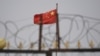 FILE - The Chinese flag flutters behind razor wire at a housing compound in Yangisar, south of Kashgar, in China's western Xinjiang region, June 4, 2019.