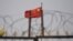 FILE - The Chinese flag flutters behind razor wire at a housing compound in Yangisar, south of Kashgar, in China's western Xinjiang region, June 4, 2019.