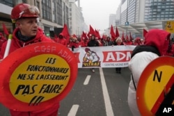 Seorang anggota serikat pekerja memegang tanda bertuliskan "pegawai negeri tidak akan membiarkan hal itu terjadi" selama demonstrasi nasional untuk memprotes pemotongan anggaran federal di Brussels, Kamis, 13 Februari 2025. (Marius Burgelman/AP)