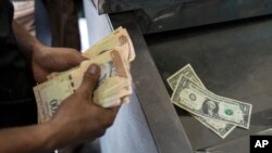 Un hombre cuenta sus bolívares y dólares para pagar artículos en un mercado en Caracas, Venezuela, el domingo 19 de mayo de 2019.