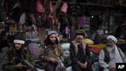 Taliban fighters sit next to street vendors at a local market in Kabul, Afghanistan, Friday, Sept. 10, 2021. (AP Photo/Felipe Dana)