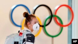 A German athlete, wearing face mask, walks past the Olympic rings display on their arrival at Haneda airport in Tokyo, July 1, 2021. 