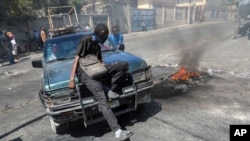 Un manifestante se sienta sobre el capó de un automóvil durante una manifestación para exigir acciones gubernamentales contra la violencia de pandillas en Puerto Príncipe, Haití, el jueves 20 de febrero de 2025.