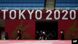 Sejumlah anggota staf berjalan di bawah logo Tokyo 2020 di arena laga Judo di Nippon Budokan menjelang pembukaan Olimpiade Musim Panas 2020, di Tokyo, Jumat, 23 Juli 2021. (AP Photo/Vincent Thian)