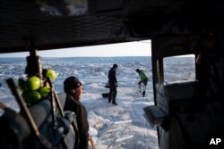 FILE - NYU air and ocean scientist David Holland and field safety officer Brian Rougeux are helped by pilot Martin Norregaard as they carry antennas out of a helicopter at the Helheim glacier, in Greenland, Aug. 16, 2019.