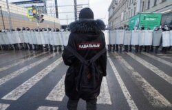 Un hombre con un letrero que dice 'Navalny' en la espalda se para frente a policías antidisturbios que bloquean el camino a una protesta contra el encarcelamiento del líder opositor Alexei Navalny en San Petersburgo, Rusia, el 31 de enero de 2021.