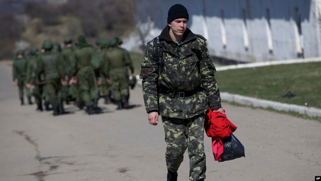 Seorang tentara Ukraina berjalan melewati tentara Rusia yang tengah berbaris menuju barak mereka di luar markas militer di Perevalne, Krimea, 21 Maret 2014. 