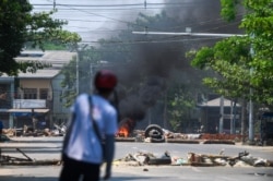 A resident looks at a burning barricade, erected by protesters then set on fire by soldiers, during a crackdown on demonstrations against the military coup in Insein township in Yangon on March 10, 2021. (Photo by STR / AFP)