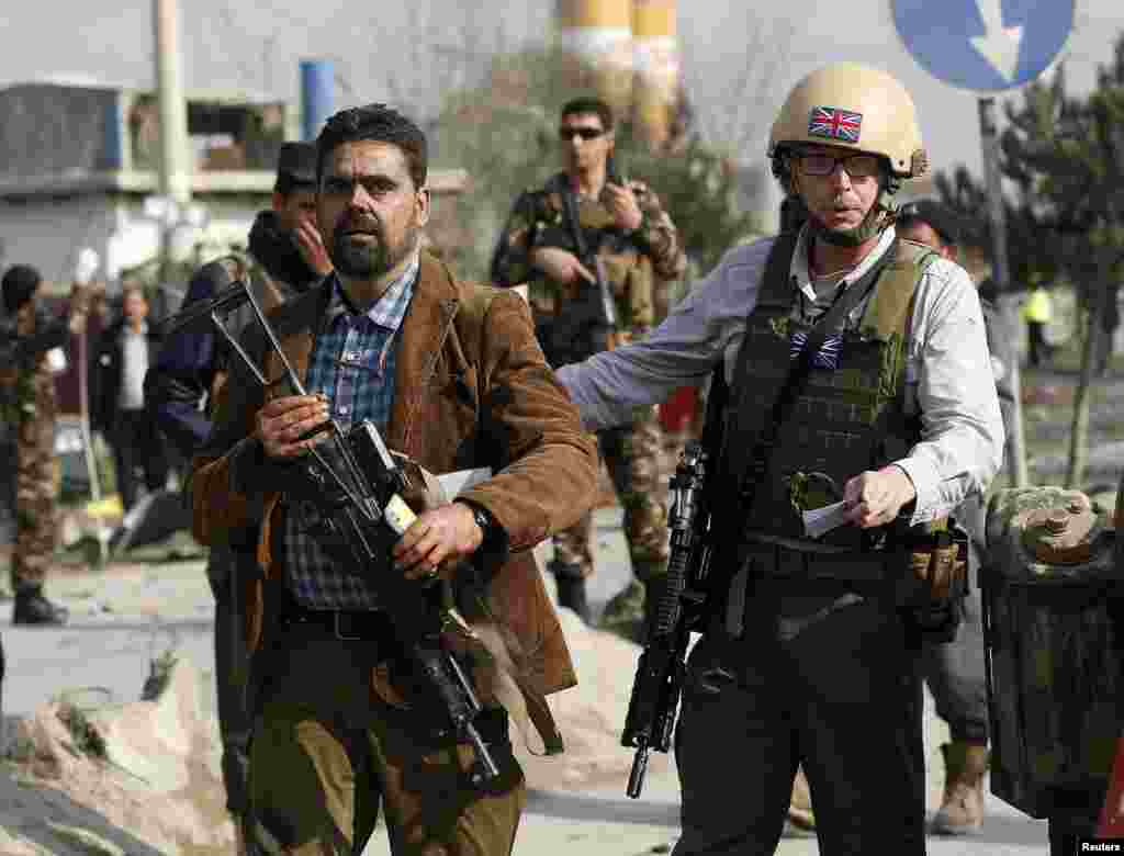 A British security official, right, escorts a survivor from the wreckage of a British embassy vehicle after a suicide attack in Kabul, Nov. 27, 2014.