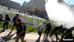 Demonstrators run away from a jet of water released by a riot police vehicle during a protest calling for changes in the education system in Santiago, Chile, April 11, 2017.