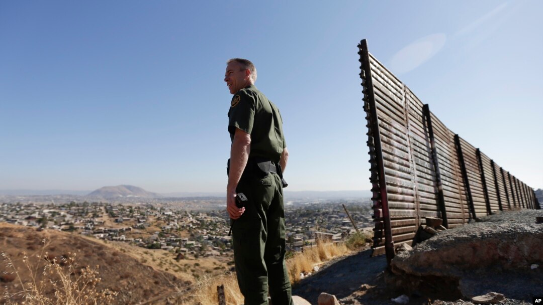 In this June 13, 2013 file photo, US Border Patrol agent Jerry Conlin looks out over Tijuana, Mexico, behind, along the old border wall along the US - Mexico border, where it ends at the base of a hill in San Diego.