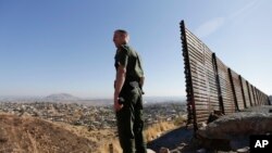 In this June 13, 2013 file photo, US Border Patrol agent Jerry Conlin looks out over Tijuana, Mexico, behind, along the old border wall along the US - Mexico border, where it ends at the base of a hill in San Diego.
