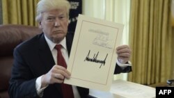 El presidente Donald J. Trump muestra un documento el día de la firma de la Ley de Recorte y Reforma de Impuestos en la Oficina Oval, el 22 de diciembre de 2017.