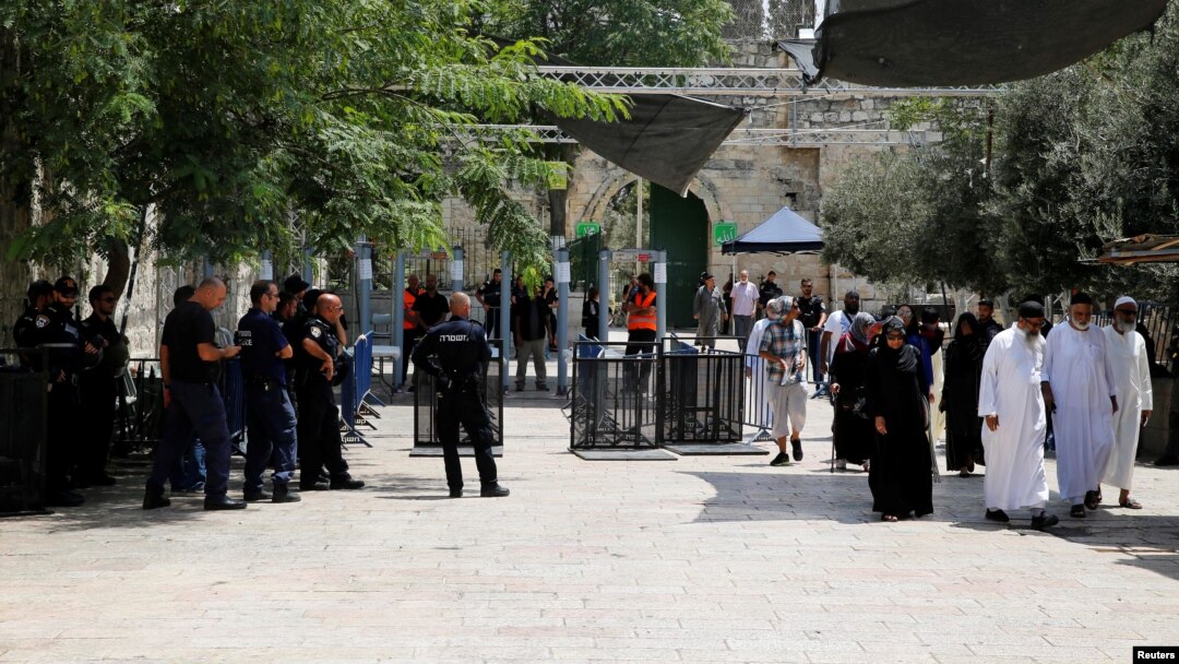 Tourists walk near Israeli police officers and recently installed metal detectors at an entrance to the compound known to Muslims as Noble Sanctuary and to Jews as Temple Mount in Jerusalem's Old City, July 23, 2017. 
