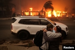 People embrace as they evacuate following powerful winds fueling devastating wildfires in the Los Angeles area, at the Eaton Fire in Altadena, California, Jan. 8, 2025.