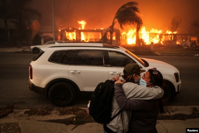 People embrace as they evacuate following powerful winds fueling devastating wildfires in the Los Angeles area, at the Eaton Fire in Altadena, California, Jan. 8, 2025.