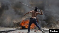 A Palestinian protester uses a sling to hurl stones toward Israeli troops near the Jewish settlement of Bet El, near the occupied West Bank city of Ramallah, Oct. 5, 2015. 