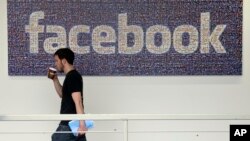 FILE - An employee walks past a sign at Facebook headquarters in Menlo Park, California, March 15, 2013. The social media giant is opening a new London office Monday.