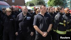 Integrantes de servicios de emergencia asisiten a un minuto de silencio por las víctimas del incendio en el edificio Grenfell, cerca del sitio del incendio en North Kesington, Londres, el lunes, 19 de junio de 2017.
