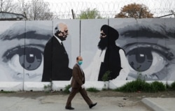 FILE - An Afghan man wearing a protective face mask walks past a mural depicting U.S. peace envoy for Afghanistan Zalmay Khalilzad, left, and Taliban chief negotiator Mullah Abdul Ghani Baradar, in Kabul, Afghanistan, April 13, 2020.