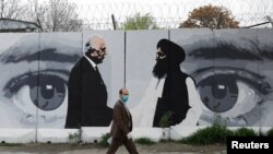 FILE - An Afghan man wearing a protective face mask walks past a mural depicting U.S. peace envoy for Afghanistan Zalmay Khalilzad, left, and Taliban chief negotiator Mullah Abdul Ghani Baradar, in Kabul, Afghanistan, April 13, 2020.