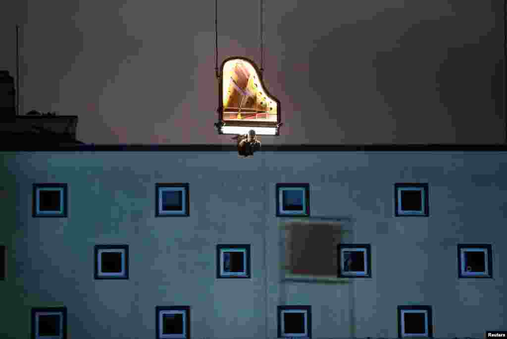 Swiss artist Alain Roche plays the piano hanging from a crane during a concert at a construction site in Munich, Germany.