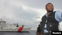 Un guardia costero jamaiquino vigila en Puerto Antonio, con el fondo de un guardacostas de Estados Unidos.