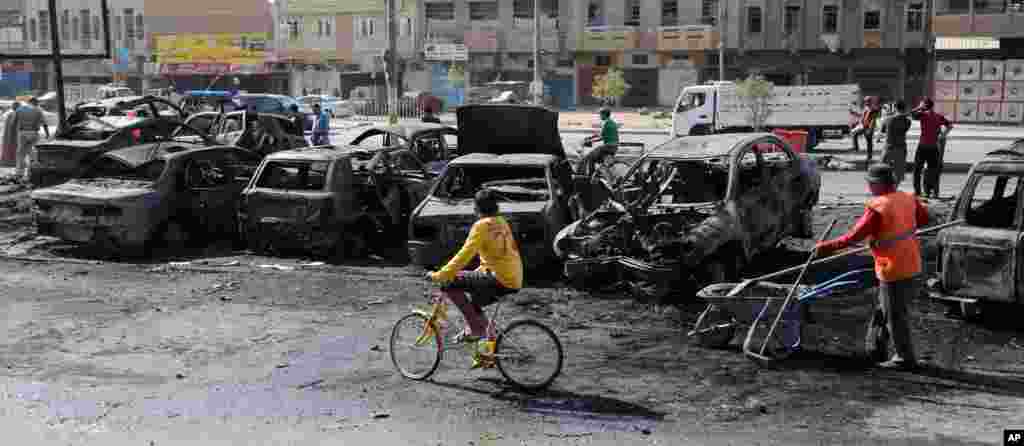 Baghdad municipality workers clear debris while people look at the site of a car bomb attack in the Sha'ab neighborhood of Baghdad, Oct. 27, 2013.